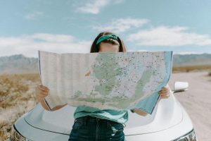 Devojka naslonjena na automobil gleda u mapu