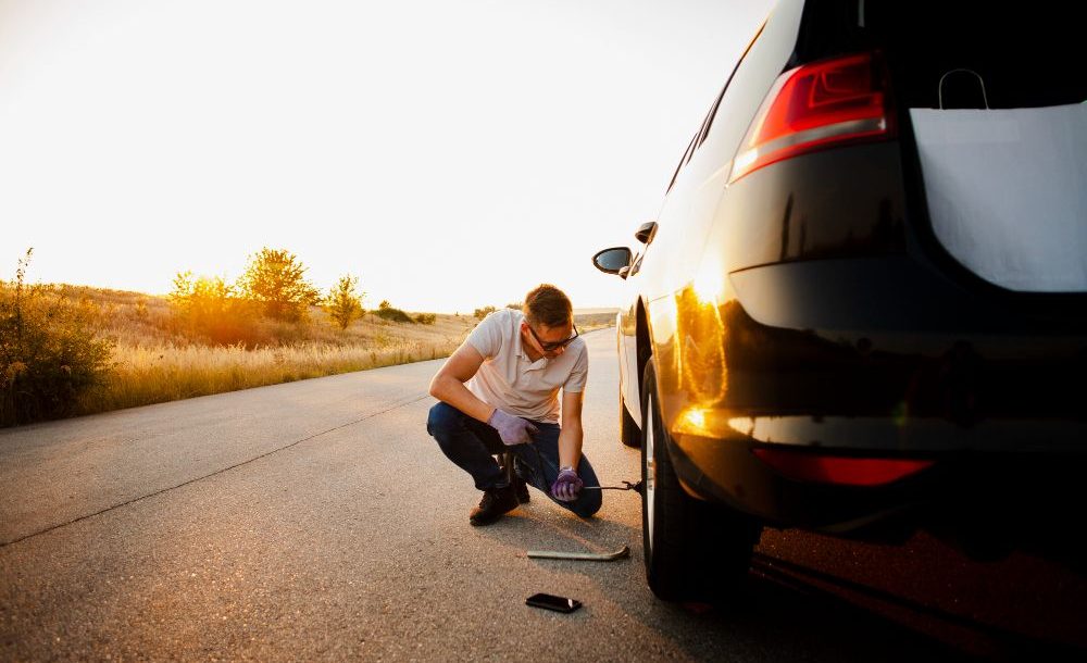 muskarac proverava gume na automobilu pred put