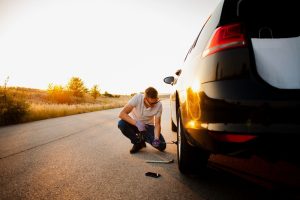 muskarac proverava gume na automobilu pred put