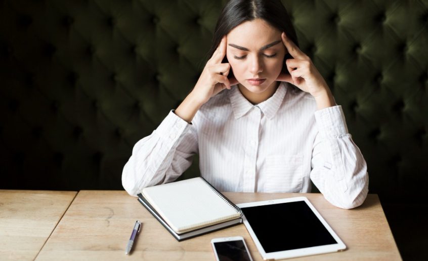 devojka sedi za stolom zatvorenih ociju i sa rukama na glavi